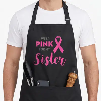 Sister crab dad apron - I WEAR PINK FOR MY Sister text and pink ribbon on grey background — shown on a black cotton canvas apron against a white background