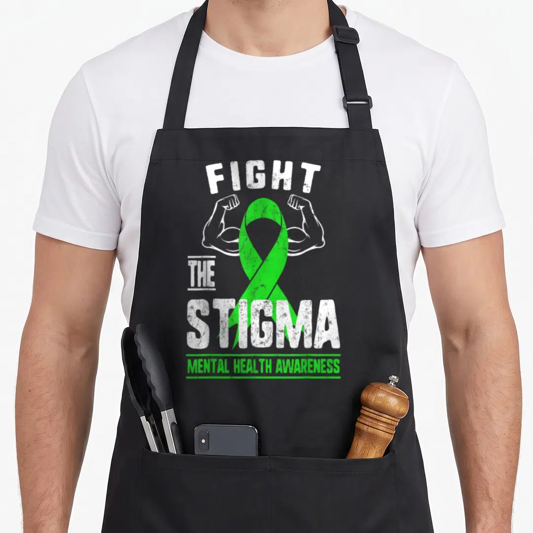 Fight anxiety apron - Green ribbon between two flexed white arms with FIGHT THE STIGMA MENTAL HEALTH AWARENESS text — shown on a black cotton canvas apron against a white background