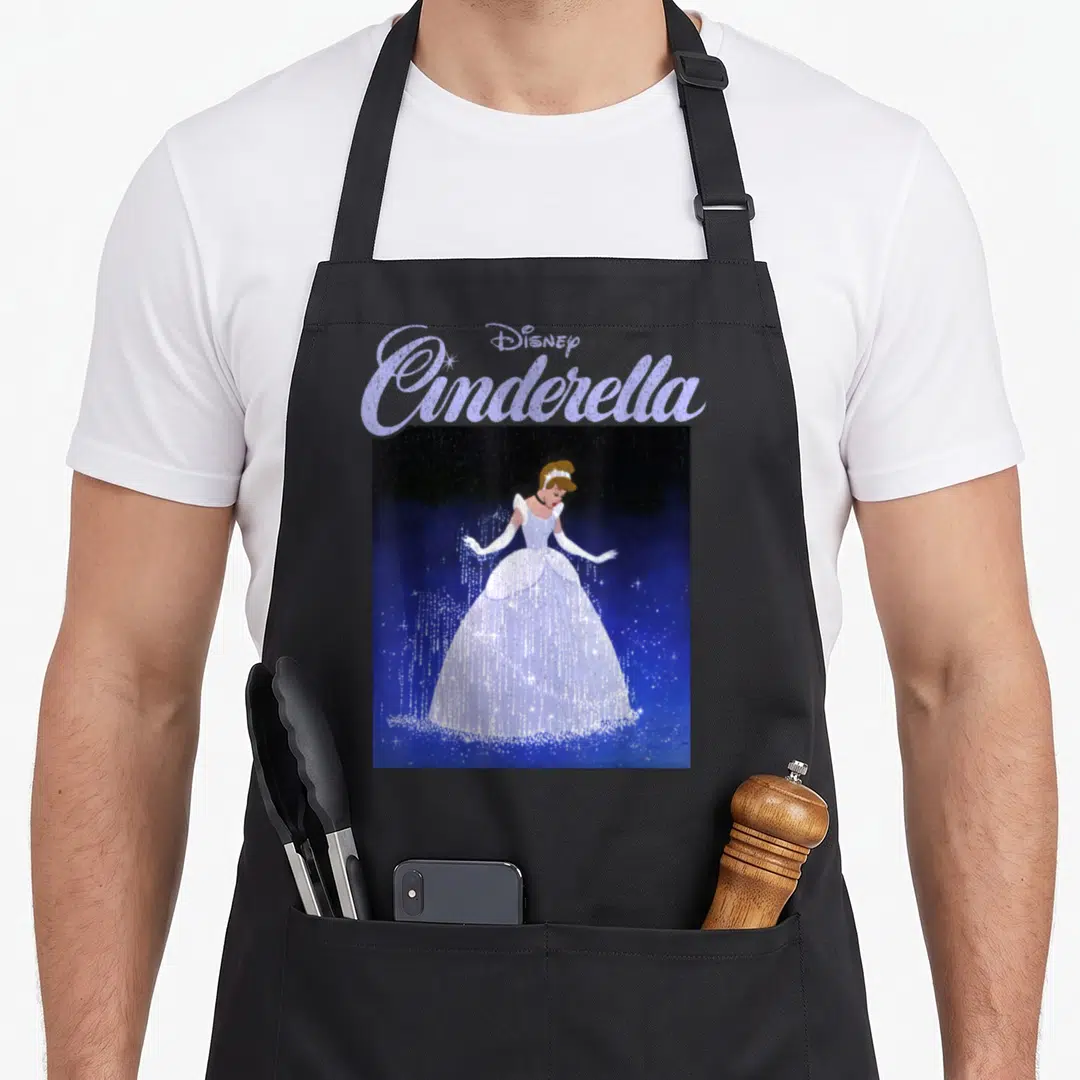 70th cinderella apron - Stacked Disney Cinderella text above a standing figure in a white dress against a starry blue — shown on a black cotton canvas apron against a white background