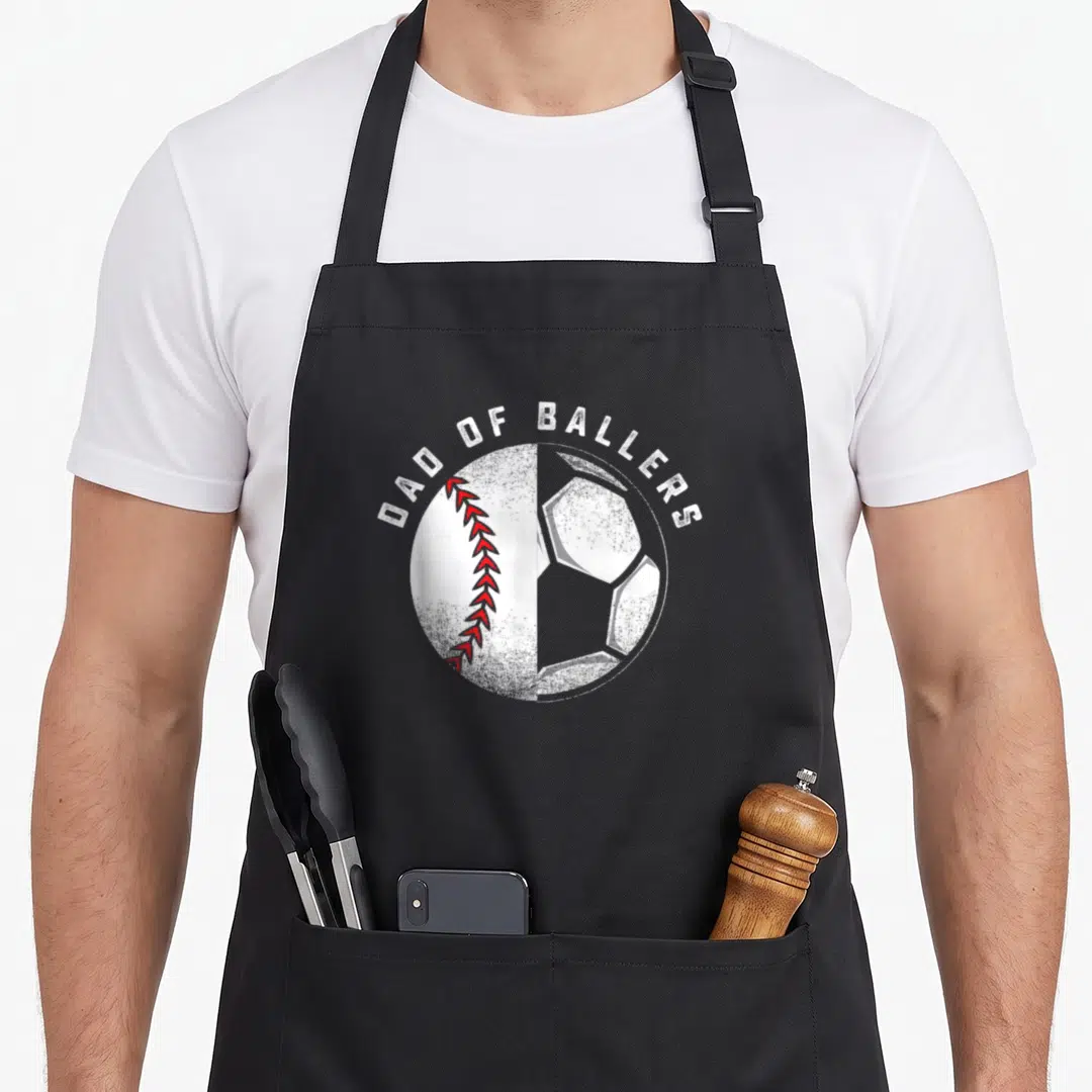 Baller father son apron - DAD OF BALLERS text over split baseball and soccer ball graphic — shown on a black cotton canvas apron against a white background