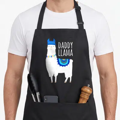 Llama daddy apron - Cartoon white llama in blue hat next to stacked DADDY LLAMA text — shown on a black cotton canvas apron against a white background
