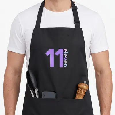 11th eleven birthday apron - Purple 11 and vertical eleven text in pink and blue typography — shown on a black cotton canvas apron against a white background