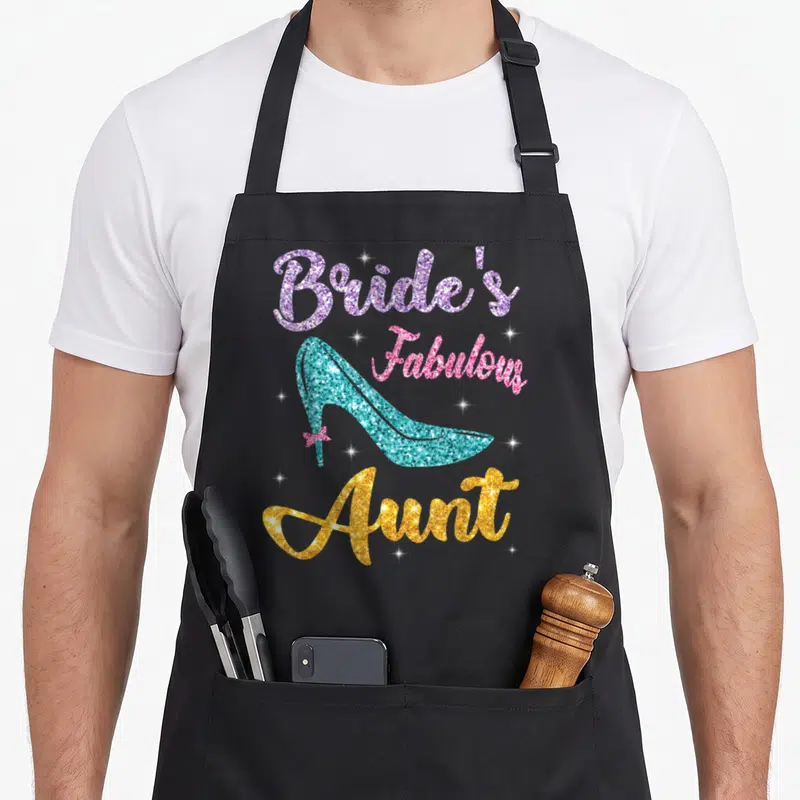 Married wedding day aprons - Bride's Fabulous Aunt text with turquoise high heel shoe and pink bow — shown on a black cotton canvas apron against a white background