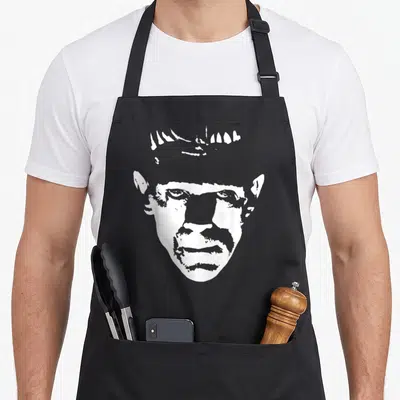 Monster frankenstein halloween apron - White line-art silhouette of a man's face with prominent forehead and ears — shown on a black cotton canvas apron against a white background