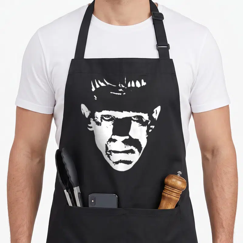 Monster frankenstein halloween apron - White line-art silhouette of a man's face with prominent forehead and ears — shown on a black cotton canvas apron against a white background