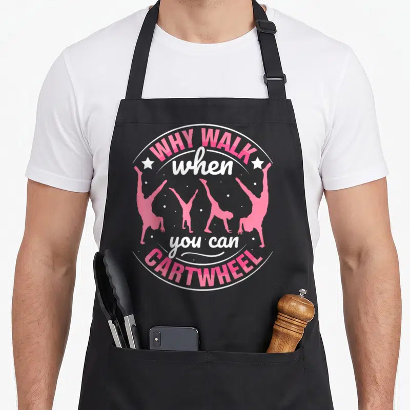 Gymnastic nourjoy apron - Why Walk When You Can Cartwheel text with four pink gymnast silhouettes in a circle — shown on a black cotton canvas apron against a white background