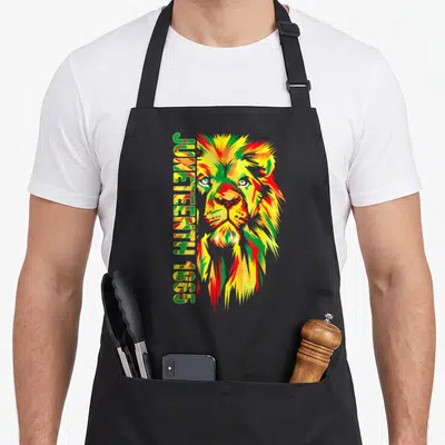 Juneteenth lion african american aprons - Cartoon lion head in green yellow red with vertical Juneteenth 1865 text — shown on a black cotton canvas apron against a white background