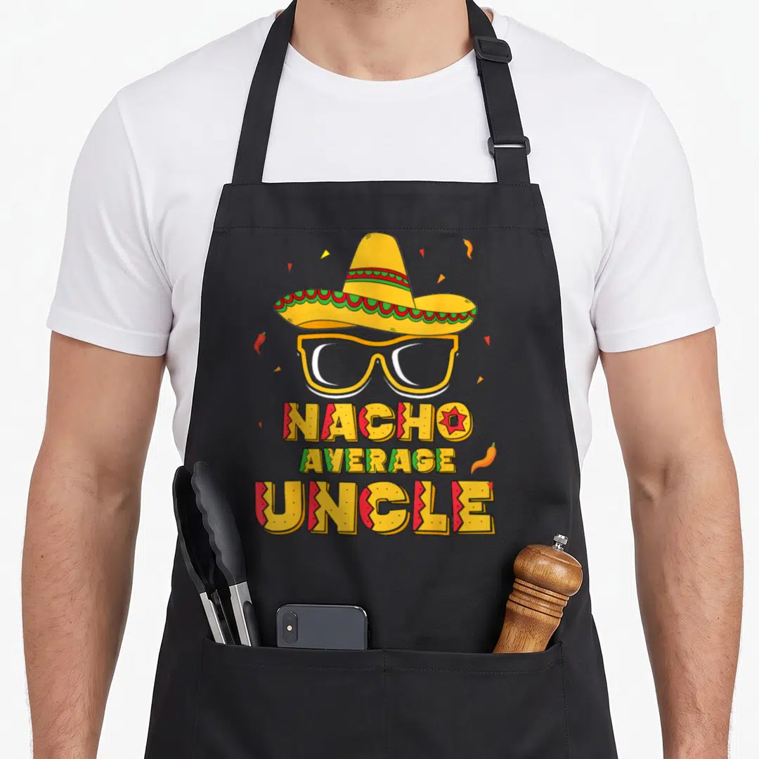Nacho mayo apron - Sombrero, glasses, NACHO AVERAGE UNCLE text, chili peppers, confetti in yellow red green — shown on a black cotton canvas apron against a white background