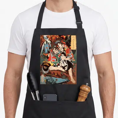 Tengu artwork apron - Two realistic figures amidst autumn leaves and water with vertical text in a yellow box — shown on a black cotton canvas apron against a white background