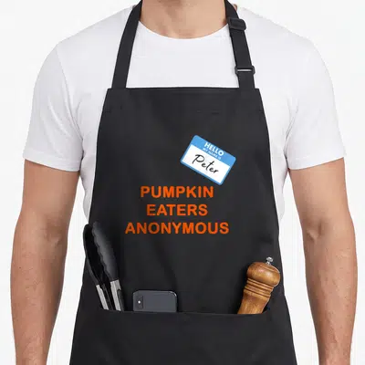 Anonymous pumpkin apron - Blue name tag reading Peter above stacked orange text Pumpkin Eaters Anonymous — shown on a black cotton canvas apron against a white background
