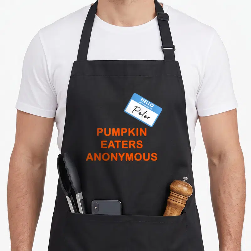 Anonymous pumpkin apron - Blue name tag reading Peter above stacked orange text Pumpkin Eaters Anonymous — shown on a black cotton canvas apron against a white background