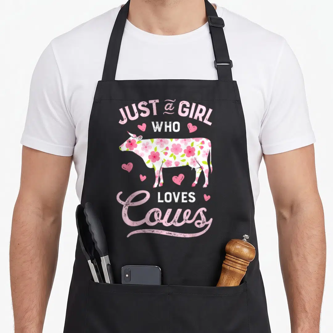 Farmer cow apron - Floral patterned cow silhouette with pink hearts and text just a girl who loves cows — shown on a black cotton canvas apron against a white background