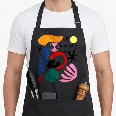 Abstract organic apron - Abstract gestural shapes in solid colors including red arc blue leaf pink fan and yellow — shown on a black cotton canvas apron against a white background