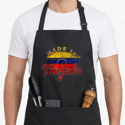 Latin venezuelan pride apron - Distressed Venezuela flag with MADE IN arched text and script country name in yellow — shown on a black cotton canvas apron against a white background