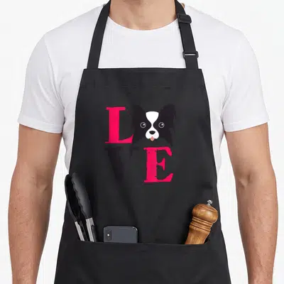 Papillion puppy dog apron - LOVE text with dog head replacing O, pink and black minimalist art — shown on a black cotton canvas apron against a white background
