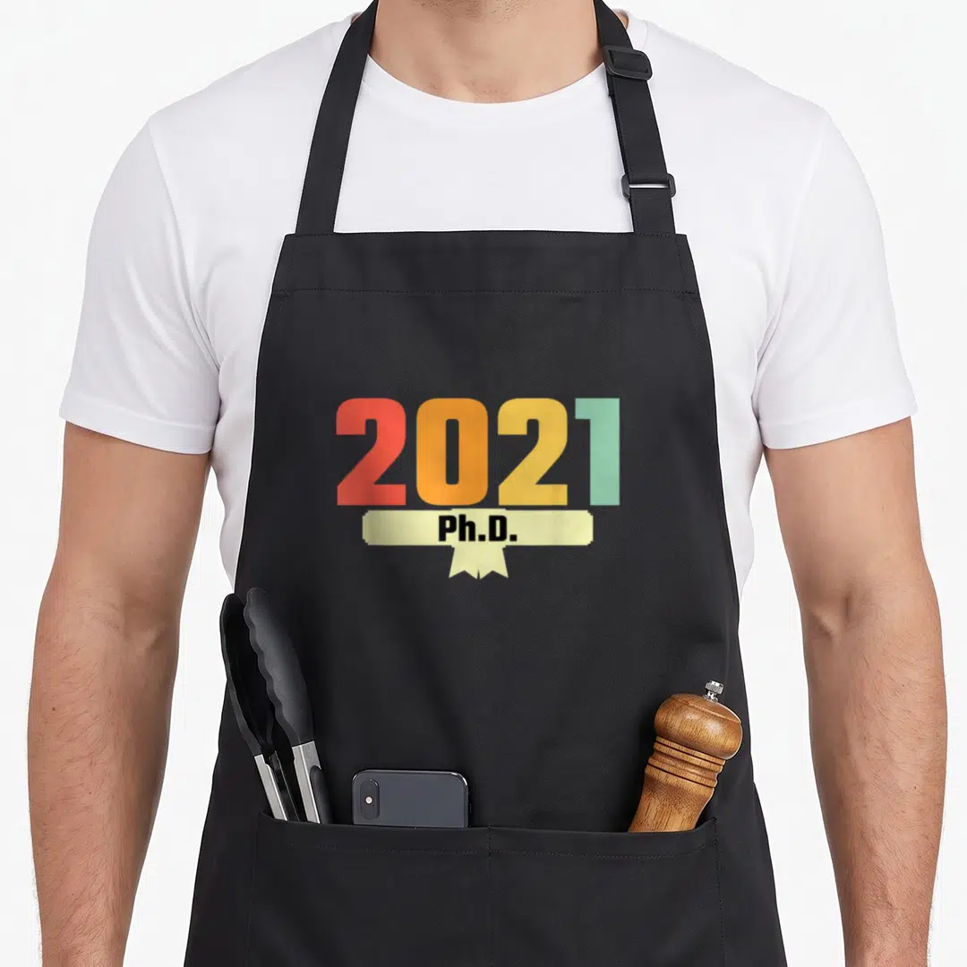 Class 70s apron - 2021 numbers in red orange yellow green with beige Ph.D ribbon — shown on a black cotton canvas apron against a white background