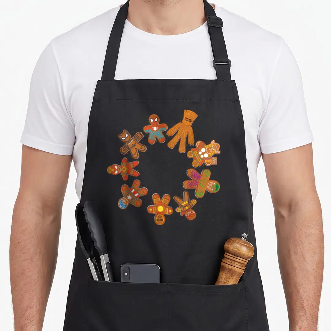 Circle gingerbread apron - Seven gingerbread superhero cookies in a ring with red blue and green icing — shown on a black cotton canvas apron against a white background