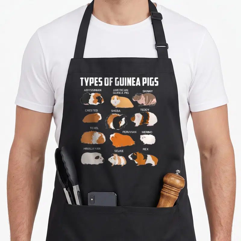Guinea different types of apron - Chart of twelve cartoon guinea pig breeds labeled Abyssinian, Teddy, Rex, and others — shown on a black cotton canvas apron against a white background