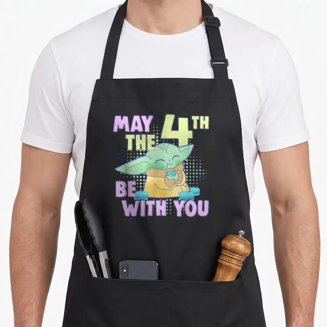 4th may apron - Grogu holding a blue heart surrounded by macarons and hearts with text MAY THE 4TH BE WITH YOU — shown on a black cotton canvas apron against a white background