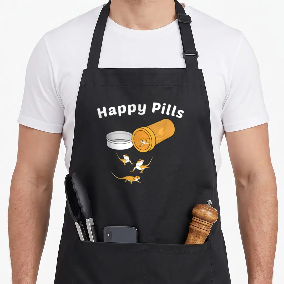 Bearded lizard dragon apron - Happy Pills text above orange pill bottle and three orange and white lizards — shown on a black cotton canvas apron against a white background