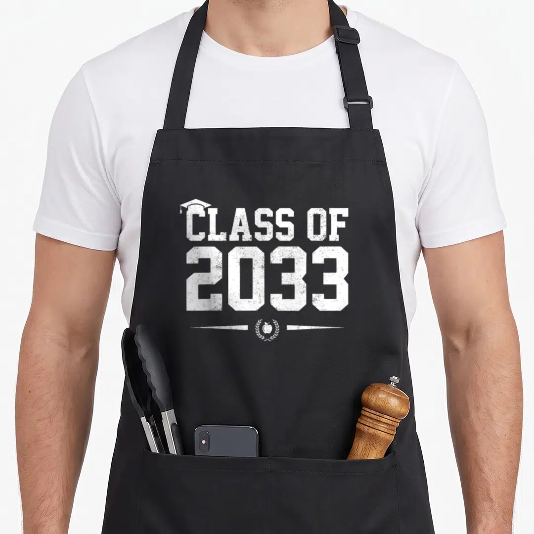 Grow graduate apron - White distressed Class of 2033 text with mortarboard and apple in laurel wreath — shown on a black cotton canvas apron against a white background
