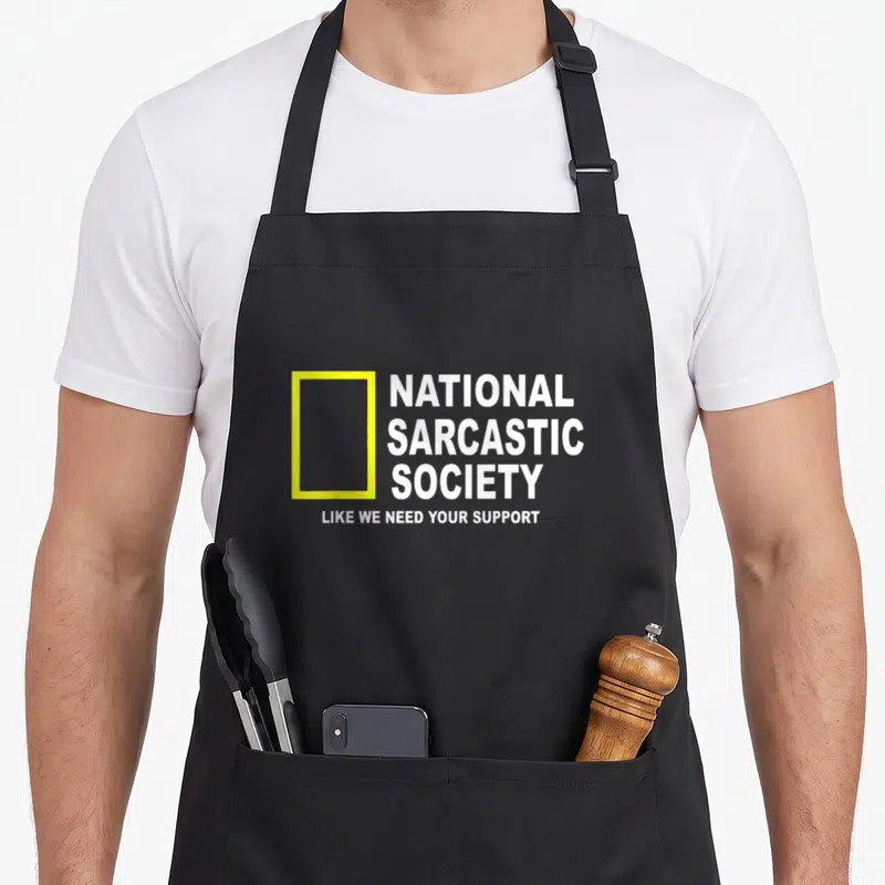 National sarcastic apron - Yellow rectangle next to stacked white text National Sarcastic Society Like We Need Your — shown on a black cotton canvas apron against a white background