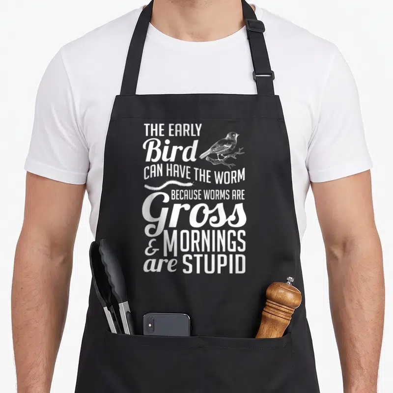 Early bird apron - White stacked text reading THE EARLY BIRD CAN HAVE THE WORM with bird and worm illustrations — shown on a black cotton canvas apron against a white background