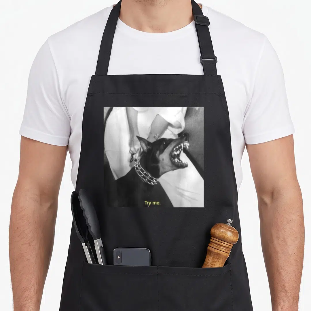 Angry doberman apron - Black white grey photo of snarling dog with person behind and centered text Try me — shown on a black cotton canvas apron against a white background