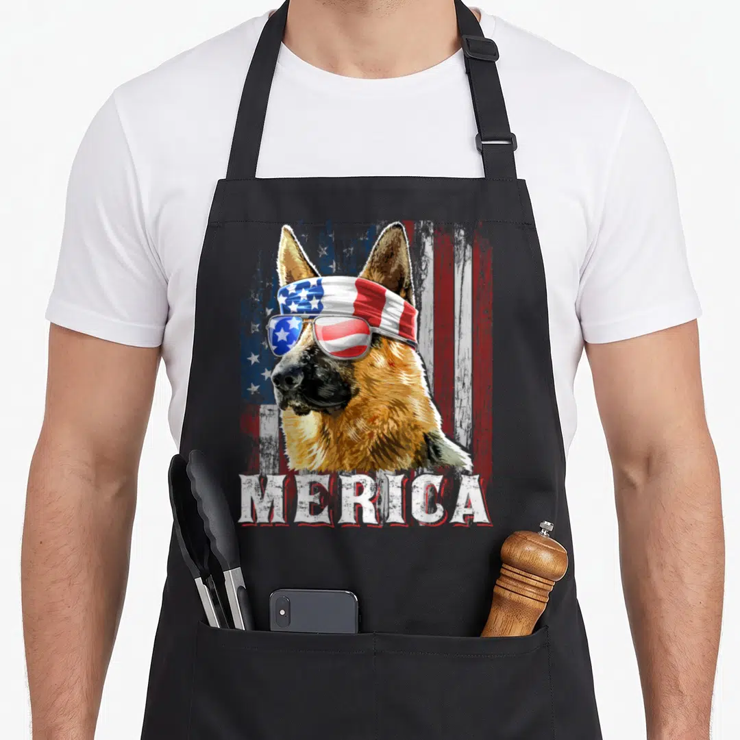 Merica dog mom apron - Realistic German Shepherd head with sunglasses and bandana over distressed red white blue flag — shown on a black cotton canvas apron against a white background
