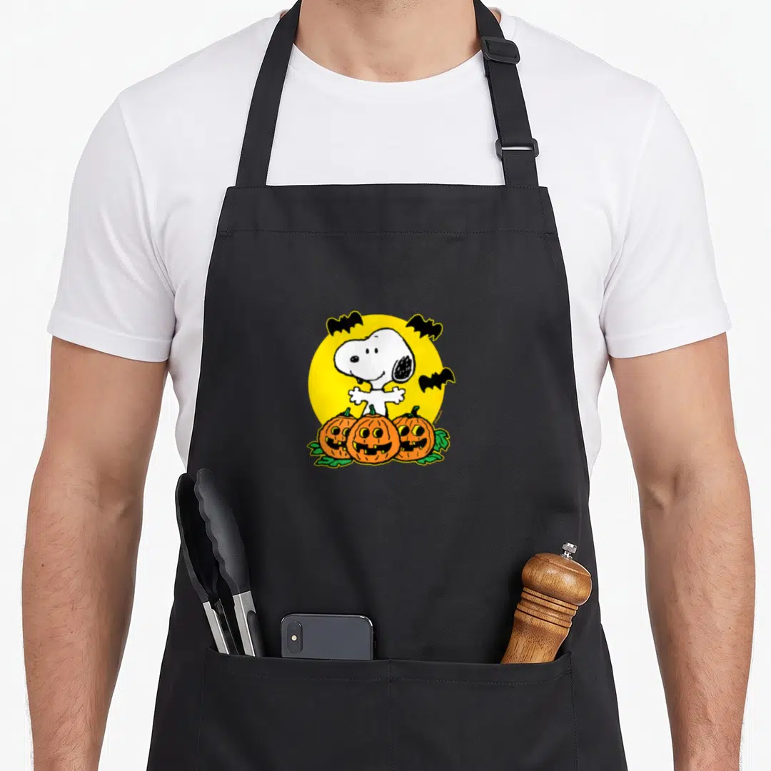 Funny pumpkin halloween apron - Snoopy standing with three bats and three pumpkins in front of a yellow circle — shown on a black cotton canvas apron against a white background