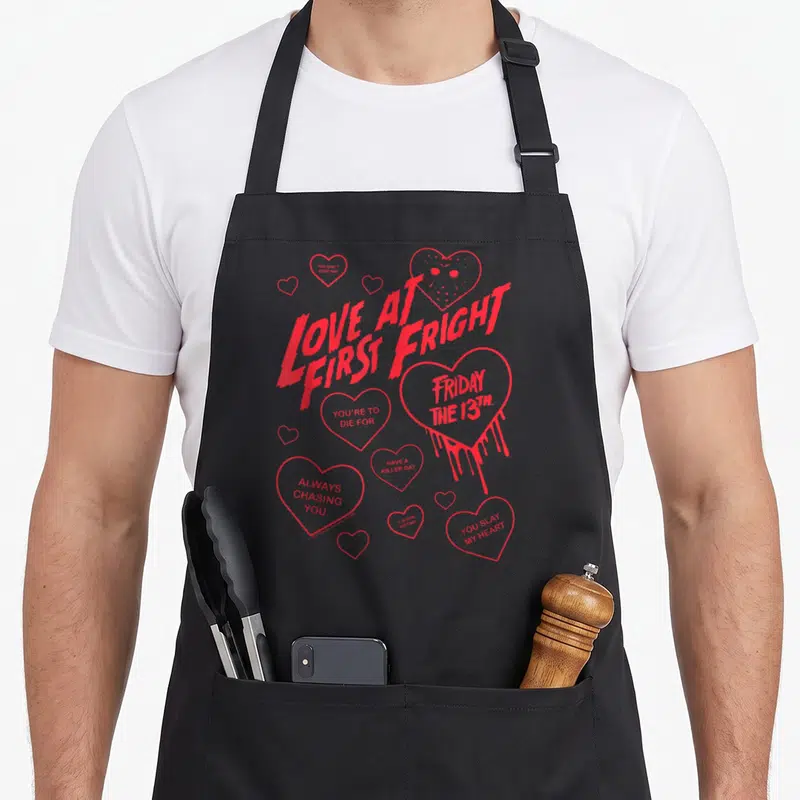Fright valentine's day apron - Red hearts with text like Love at First Fright and a hockey mask drawing — shown on a black cotton canvas apron against a white background