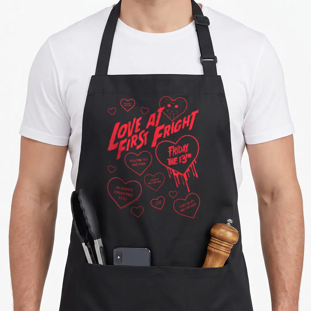 Fright valentine's day apron - Red hearts with text like Love at First Fright and a hockey mask drawing — shown on a black cotton canvas apron against a white background