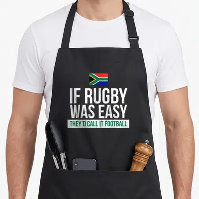 South african apron - Distressed South Africa flag above IF RUGBY WAS EASY THEY'D CALL IT FOOTBALL text — shown on a black cotton canvas apron against a white background