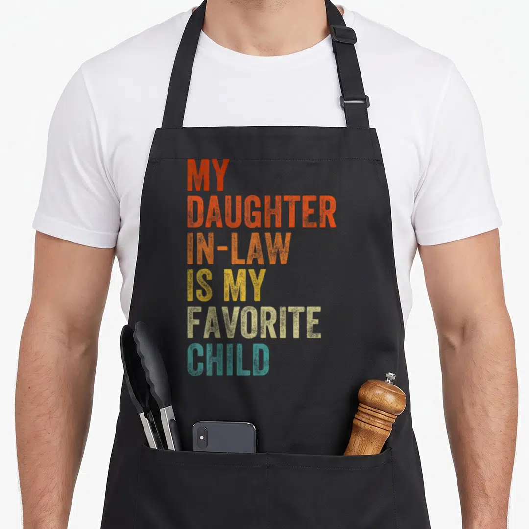 Law mother daughter apron - Stacked text MY DAUGHTER IN-LAW IS MY FAVORITE CHILD in red orange yellow beige and teal — shown on a black cotton canvas apron against a white background