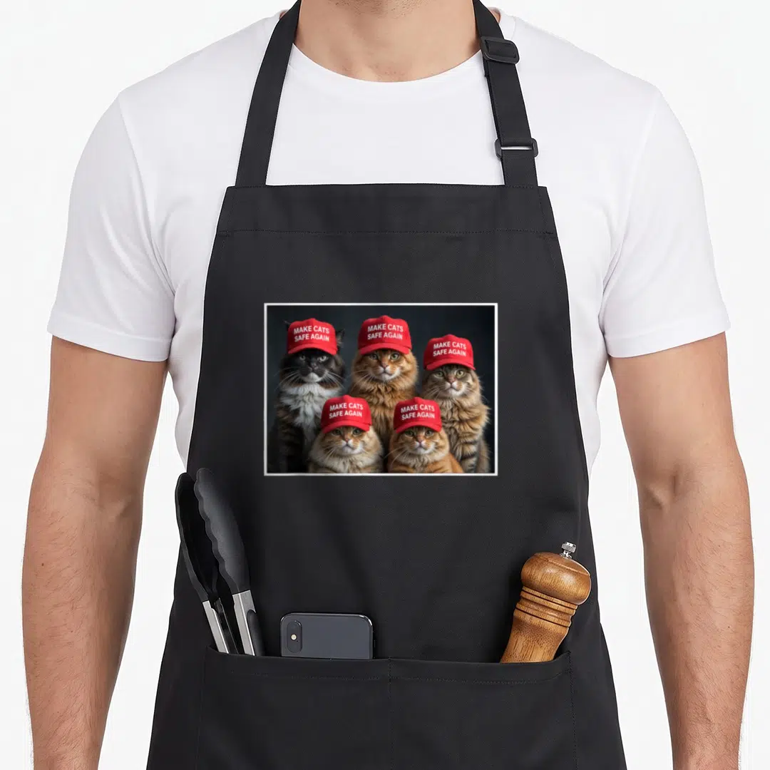 Donald cat apron - Five cats in red caps with white text reading Make Cats Safe Again — shown on a black cotton canvas apron against a white background