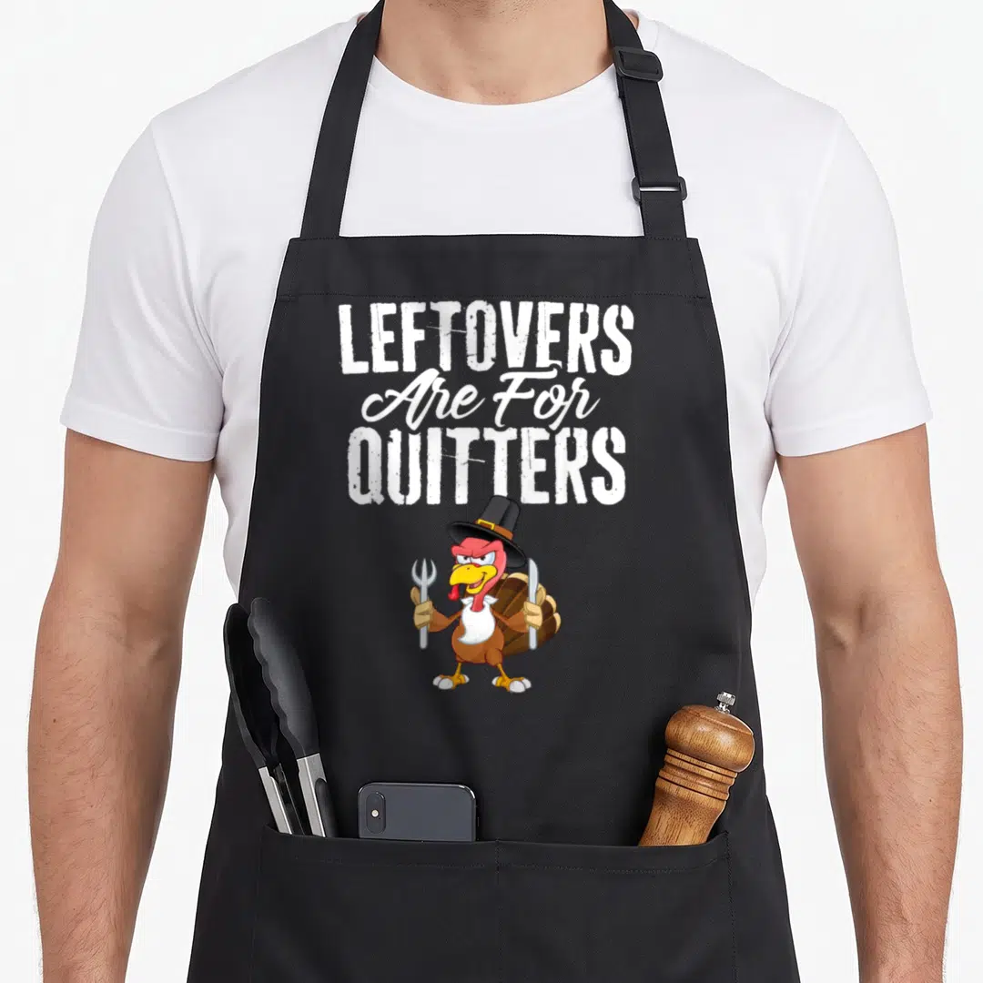 Leftover turkey apron - Cartoon turkey holding fork and knife under stacked text reading leftovers are for quitters — shown on a black cotton canvas apron against a white background