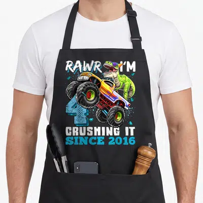 Dinosaur birthday truck apron - Green dinosaur behind yellow monster truck with blue number 4 and white text — shown on a black cotton canvas apron against a white background