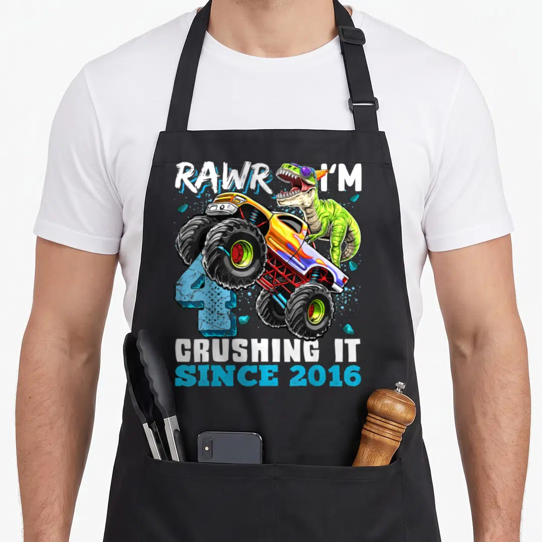 Dinosaur birthday truck apron - Green dinosaur behind yellow monster truck with blue number 4 and white text — shown on a black cotton canvas apron against a white background