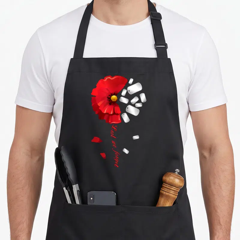 Veteran poppy apron - Red poppy merging into silver dog tags with vertical Lest we forget text — shown on a black cotton canvas apron against a white background
