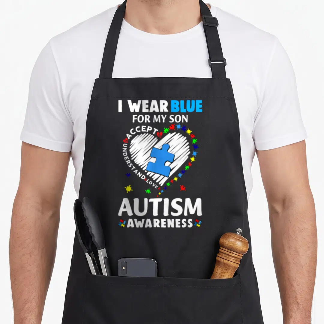 Blue nurse dad apron - I WEAR BLUE FOR MY SON text around white heart with blue puzzle piece and colorful fragments — shown on a black cotton canvas apron against a white background
