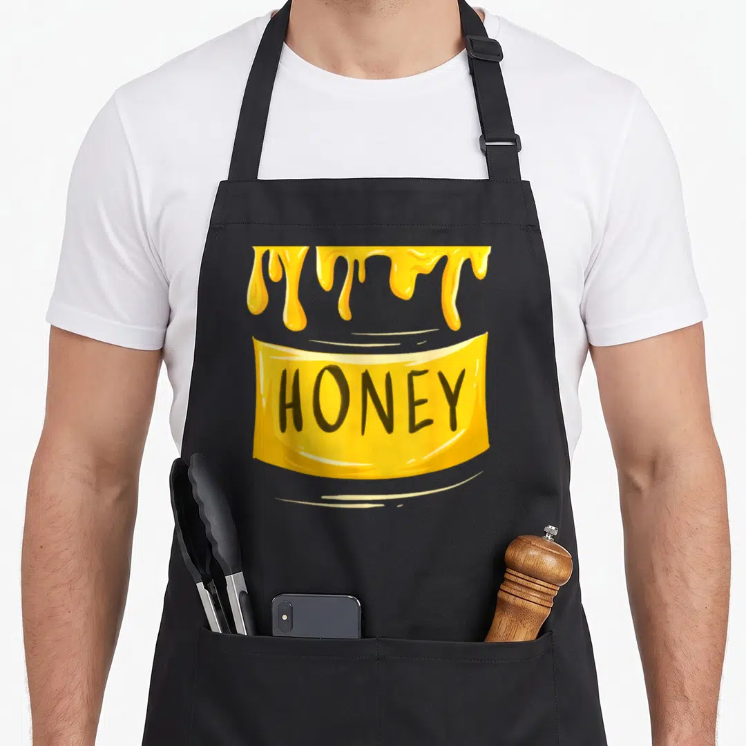 Sweet funny halloween aprons - Dripping honey above yellow banner with black HONEY text in cartoon style — shown on a black cotton canvas apron against a white background