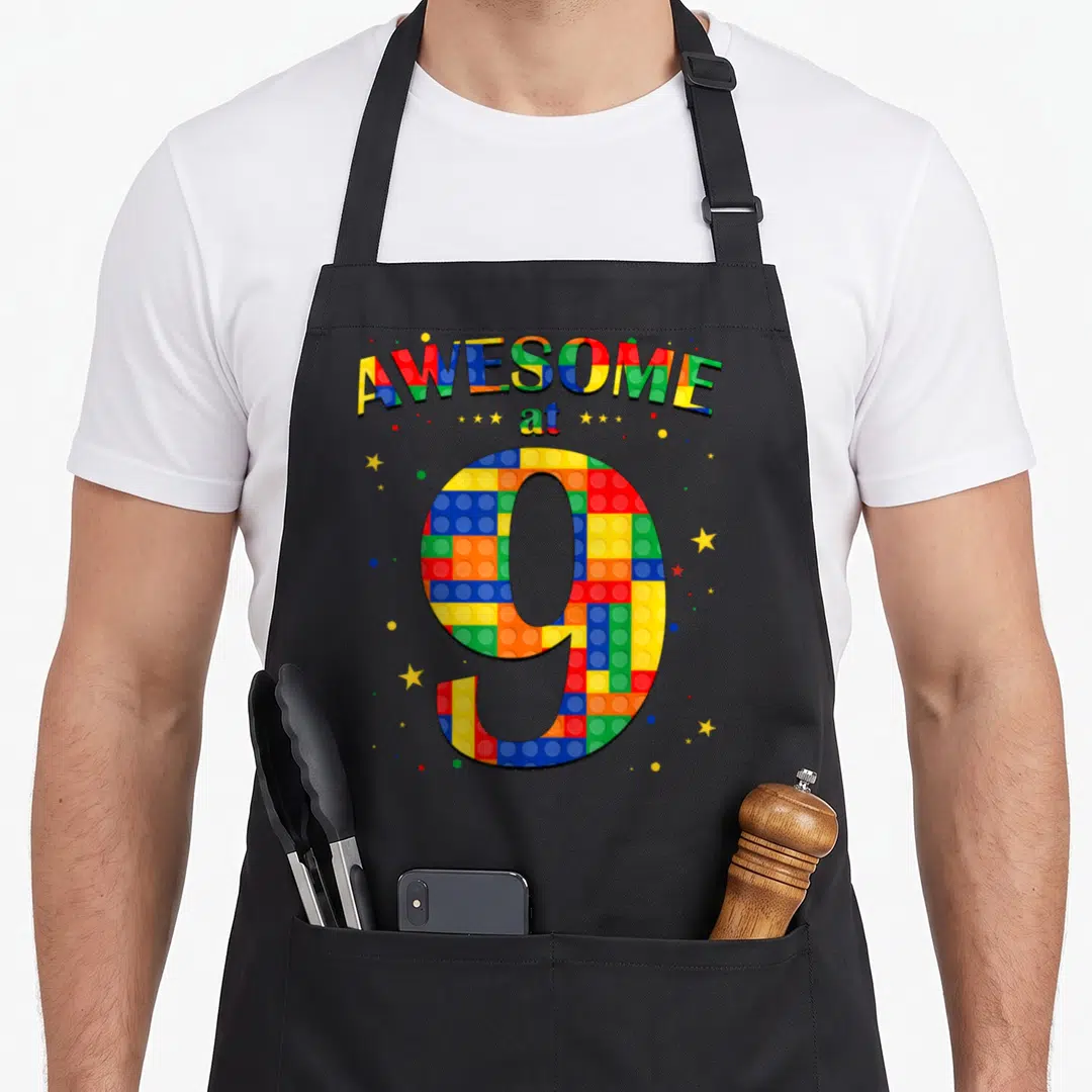 Brick birthday building aprons - Arched AWESOME at 9 text above a large number 9 filled with colorful interlocking toy — shown on a black cotton canvas apron against a white background