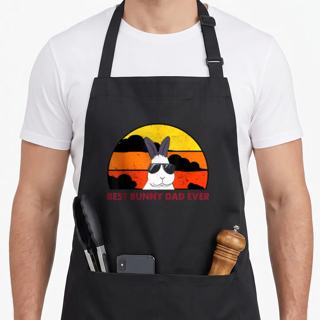 Bunny rabbit daddy apron - White bunny wearing sunglasses in front of a yellow orange and black retro sun with red text — shown on a black cotton canvas apron against a white background
