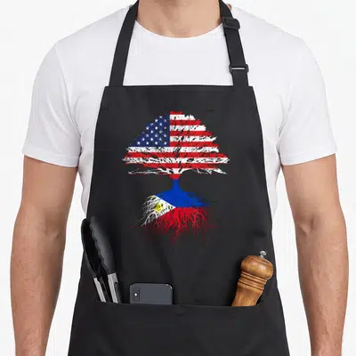 Filipino root american flag apron - Distressed tree with US flag canopy and Philippine flag roots in red white blue — shown on a black cotton canvas apron against a white background