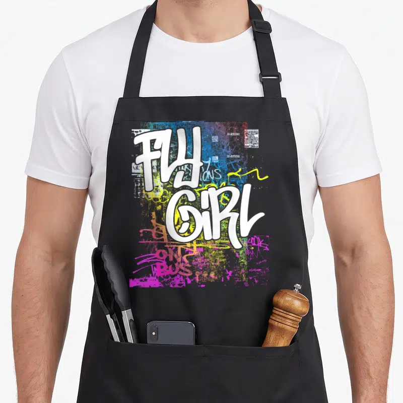 Graffiti hip apron - FLY GIRL white graffiti text over blue yellow pink green paint splatters — shown on a black cotton canvas apron against a white background