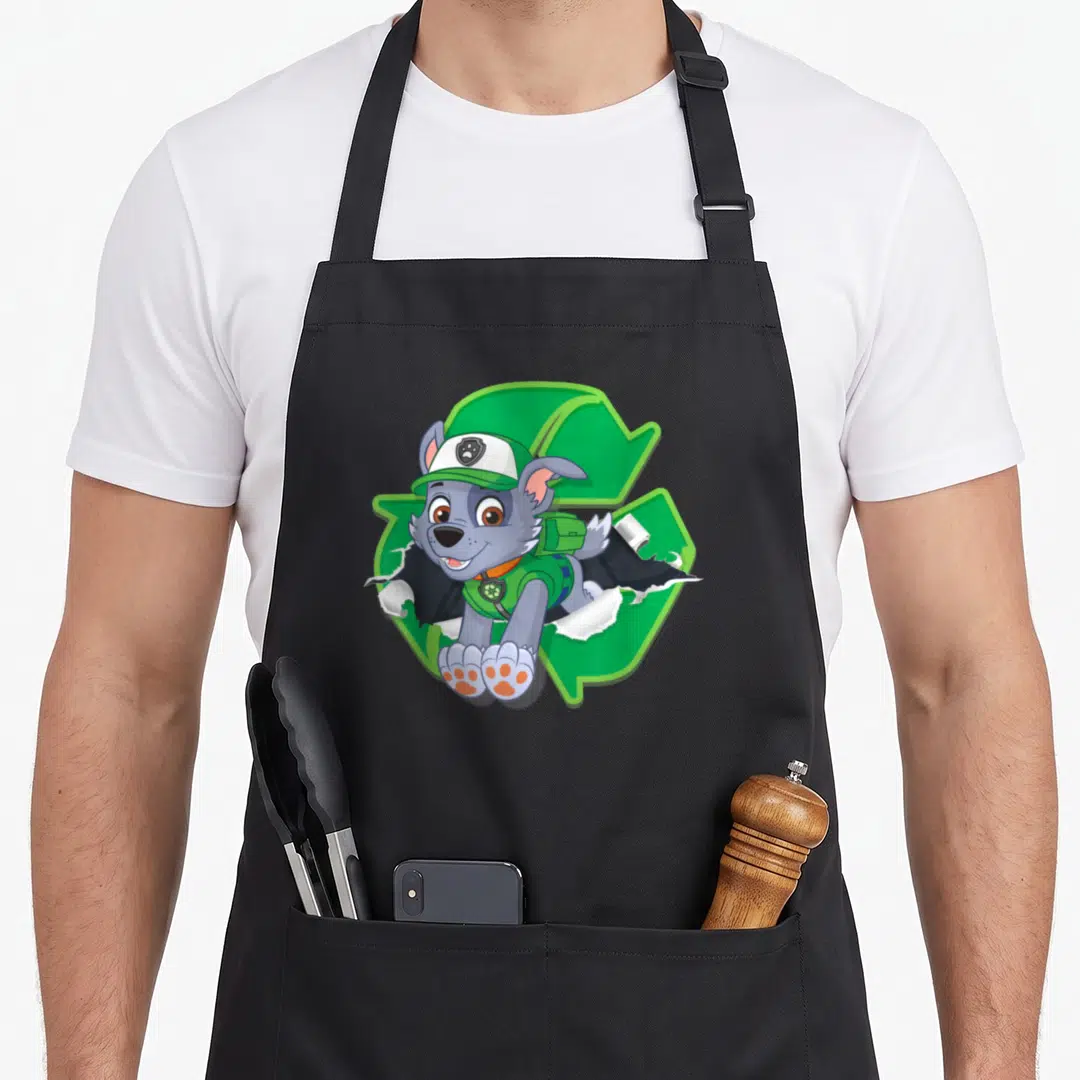 Rocky torn apron - Grey cartoon dog in hat and backpack bursting through white torn paper with green recycle symbol — shown on a black cotton canvas apron against a white background
