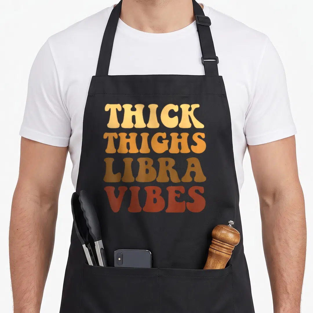 Libra thick aprons - Stacked retro text reading Thick Thighs Libra Vibes in orange and brown colors — shown on a black cotton canvas apron against a white background