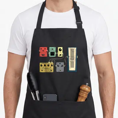 Amplifier acoustics apron - Cartoon guitar pedals in red green yellow grey blue connected to a tall amplifier — shown on a black cotton canvas apron against a white background