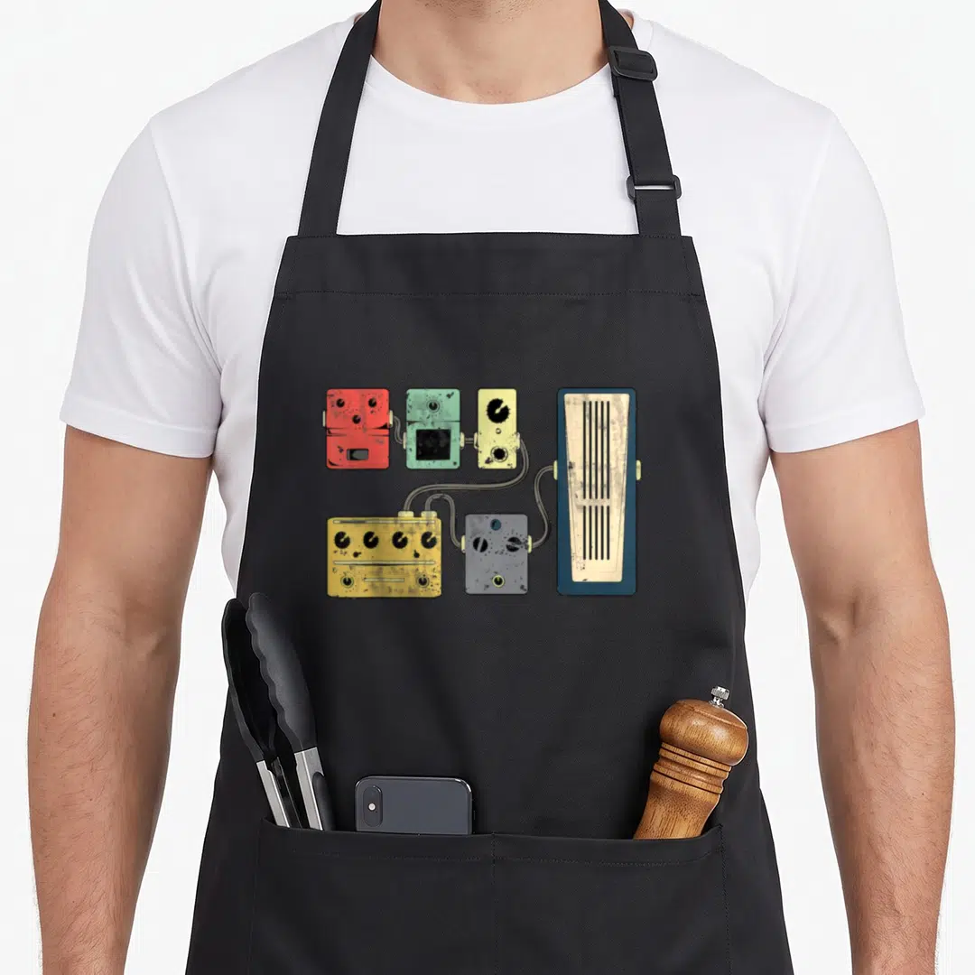 Amplifier acoustics apron - Cartoon guitar pedals in red green yellow grey blue connected to a tall amplifier — shown on a black cotton canvas apron against a white background
