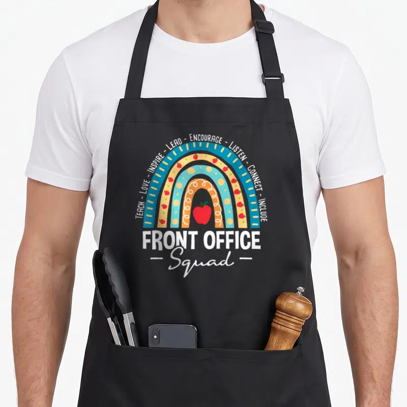 Squad school office apron - Rainbow with red apples and words TEACH LOVE INSPIRE LEAD ENCOURAGE LISTEN CONNECT INCLUDE — shown on a black cotton canvas apron against a white background